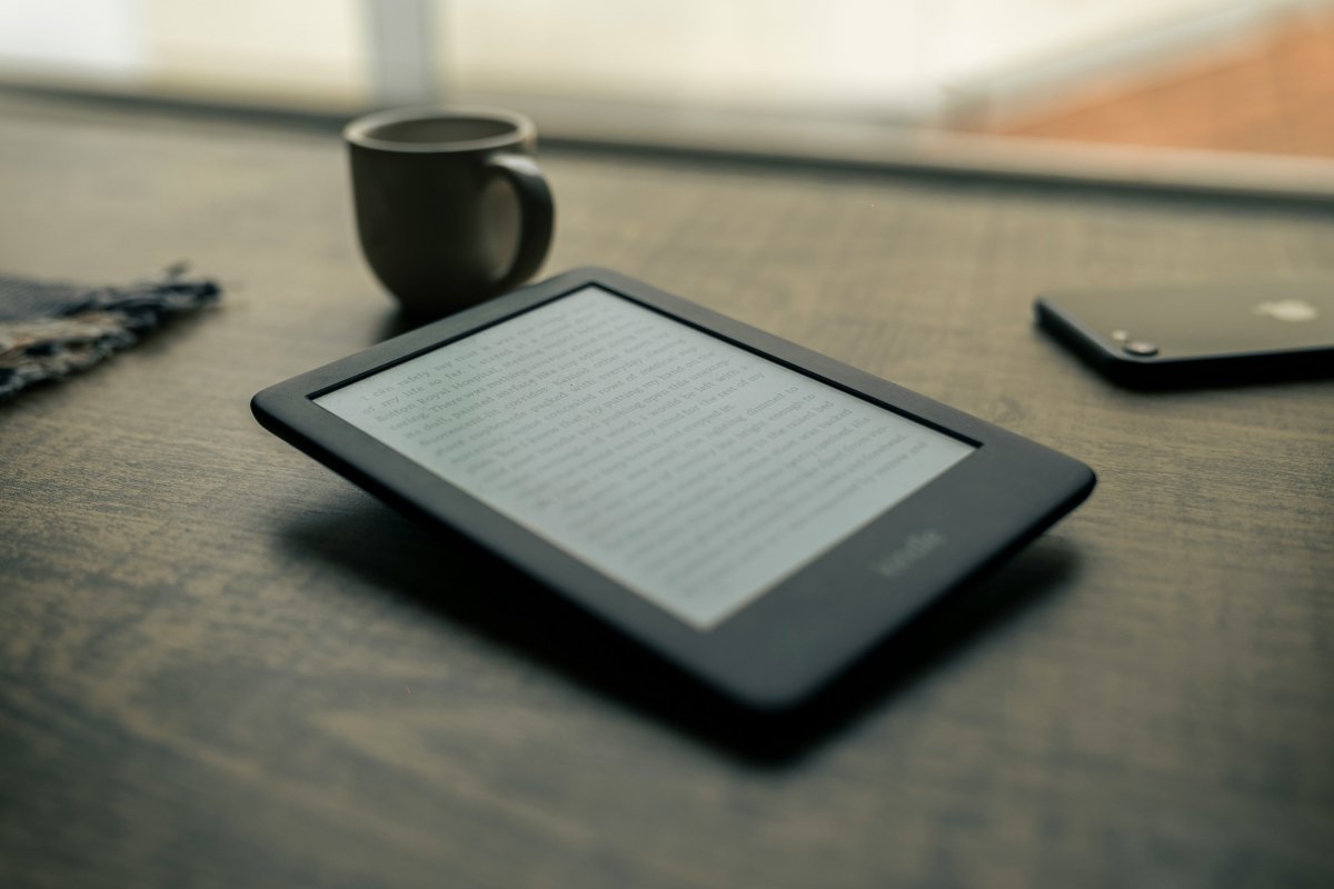 An ereader sits on a table next to a mug and phone.
